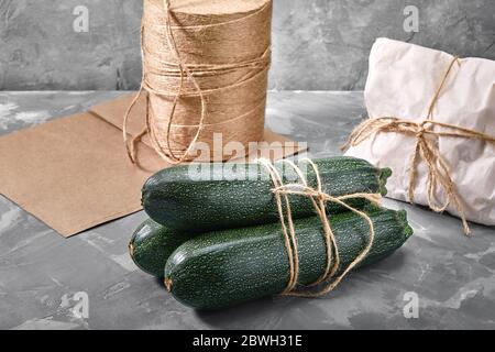 A bunch of zucchini on a gray background with a paper bag for delivery, food delivery, environmental packaging. Copy space, fresh vegetables. Stock Photo