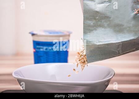 Pouring cereals in a white round bowl next to the yogurt box Stock Photo