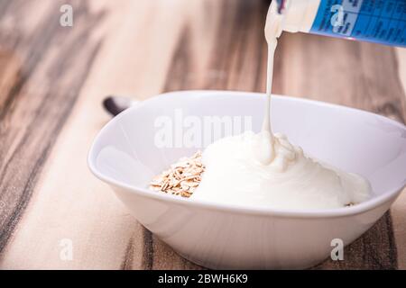 Poring natural yogurt on healthy cereals in a white round bowl Stock Photo