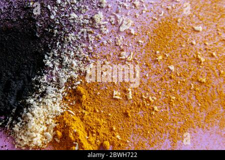 Close up explosion of black white and orange - activated carbon, coconut and turmeric on violet background Stock Photo