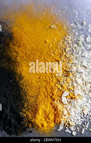 Vertical image of three color explosion of back orange and white - activated carbon, turmeric and coconut on grey background Stock Photo