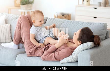 Young mother relaxing on couch with her adorable infant baby son Stock Photo