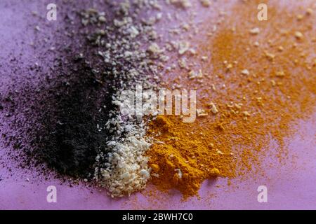 Violet background with colorful close up explosion of ingredients - activated carbon, coconut and turmeric Stock Photo