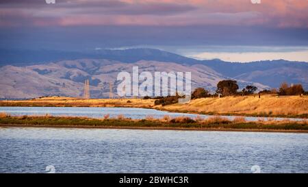 Sunset views of the restored wetlands of South San Francisco Bay Area; dark clouds covering the sky and Diablo Mountain Range visible in the backgroun Stock Photo