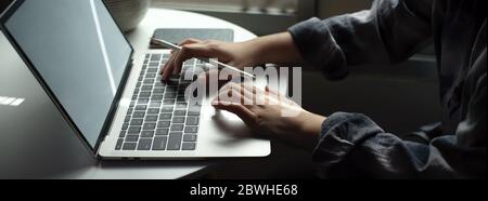 Side view of female freelancer working with laptop on circle table next to the window in living room Stock Photo