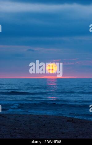 Dramatic sunset at Cavendish Beach, PEI National Park, Canada. Transient solar disk dazzles between dark storm clouds and azure ocean waters. Stock Photo