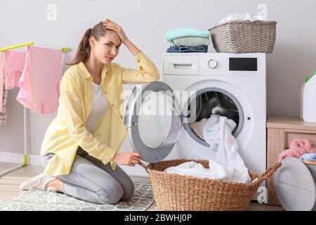 Tired young woman doing laundry in bathroom Stock Photo