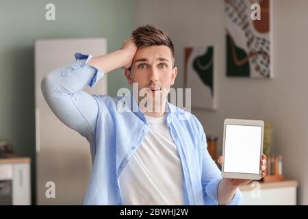 Confused man with tablet computer in kitchen at home Stock Photo