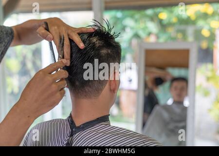 Asian young man with boy friend hairdresser trimming black hair with scissors at garden in home they stay at home during time of home isolation agains Stock Photo