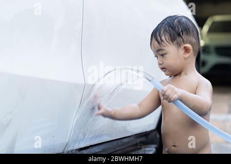 Asian child baby boy washing car, wash with luxury white car at home, in the garden on summer day. Stock Photo