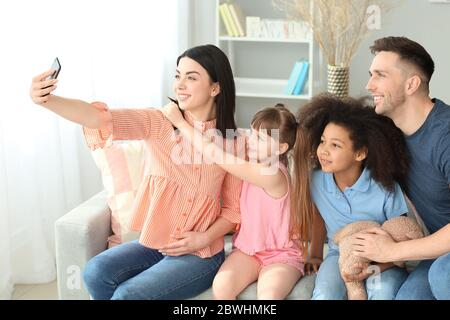 Happy couple with little adopted children taking selfie at home Stock Photo