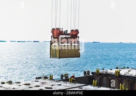 container box lifted up by spreader hang in the sky with sea background. Stock Photo