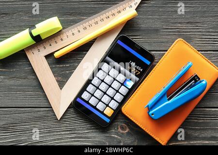 Calculator mobile application on screen of phone and stationery on dark wooden background Stock Photo