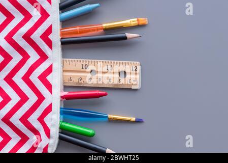Close-up of pencil case filled with child's school supplies spilling onto table. Gray background with copy space. Stock Photo