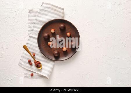 Plate with tasty chocolate candies and hazelnuts on white background Stock Photo