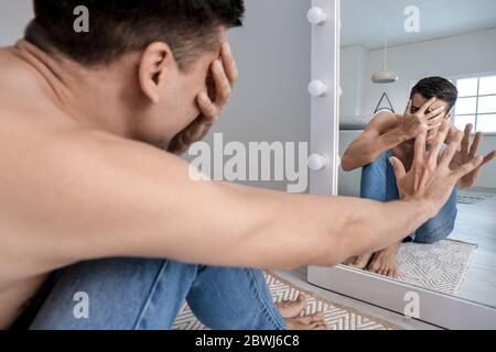 Displeased man with anorexia near mirror at home Stock Photo