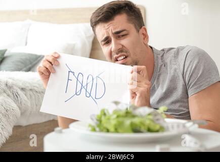 Young man suffering from anorexia and plate with salad at home Stock Photo