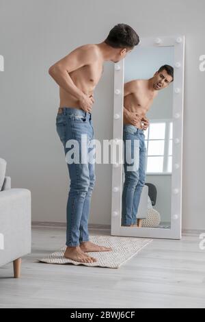 Young man with anorexia looking on his reflection in mirror at home Stock Photo