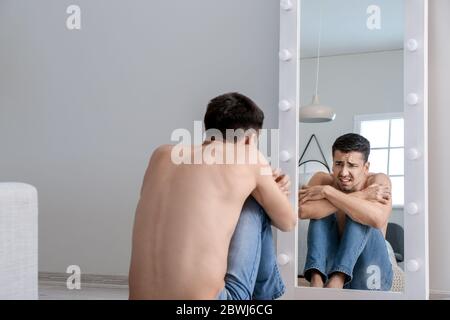 Young man with anorexia looking on his reflection in mirror at home Stock Photo