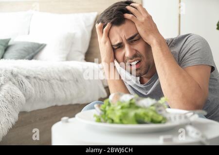 Young man suffering from anorexia and plate with salad at home Stock Photo