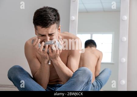 Young man suffering from anorexia with measuring tape at home Stock Photo