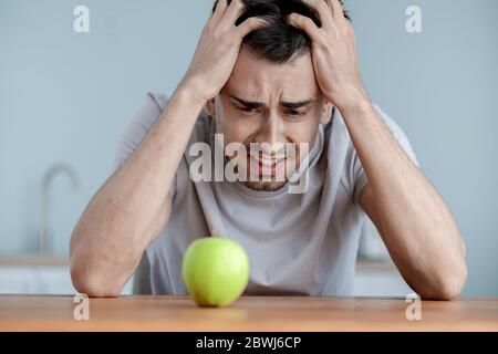 Young man suffering from anorexia with apple in kitchen Stock Photo