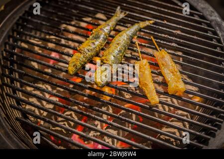 Fish grilling on a barbecue with lemon slices and rosemary with fish skewer on hot coal, outdoors barbecue Stock Photo