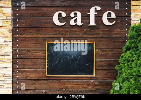 School dirty and scratched wooden Board in a frame on a wooden wall, with the inscription CAFE. Stock Photo