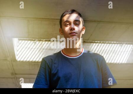 Teenager posing with light and shadow on his face in a low angle view as he looks down at the camera with a pensive expression Stock Photo