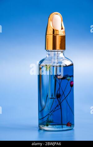 Dropper glass Bottle with flowers inside Mock-Up. Cosmetic pipette on blue background. Cuticle oil Stock Photo