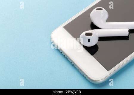 Wireless bluetooth headphones with a modern mobile phone on a blue background. The concept of modern technology, gadgets. Stock Photo