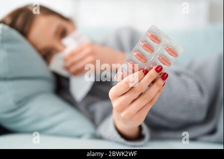 Sick Woman using paper tissue and holding pills. Flu. Sneezing into handkerchief. Headache. Virus .Medicines. Female Infected, blowing nose. Girl with Stock Photo