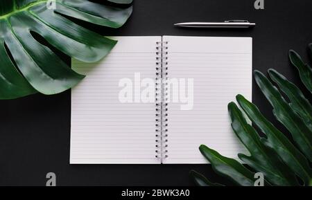 Blank white notepaper with tropical leaves laying on black table.Home office,workspace design backgrounds,flat lay,top view Stock Photo