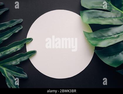 Blank white notepaper with tropical leaves laying on black table.Home office,workspace design backgrounds,flat lay,top view Stock Photo
