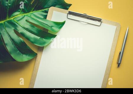 Blank white notepaper with tropical leaves laying on yellow table.Home office,workspace design backgrounds,flat lay,top view Stock Photo