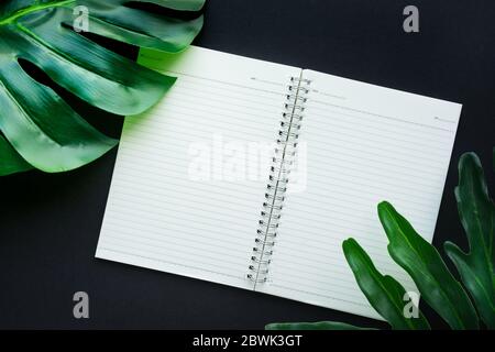Blank white notepaper with tropical leaves laying on black table.Home office,workspace design backgrounds,flat lay,top view Stock Photo
