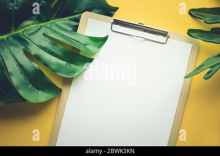 Blank white notepaper with tropical leaves laying on yellow table.Home office,workspace design backgrounds,flat lay,top view Stock Photo