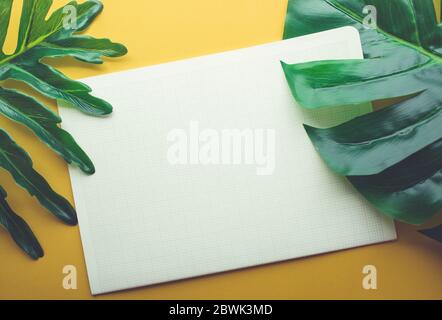 Blank white notepaper with tropical leaves laying on yellow table.Home office,workspace design backgrounds,flat lay,top view Stock Photo