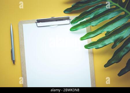 Blank white notepaper with tropical leaves laying on yellow table.Home office,workspace design backgrounds,flat lay,top view Stock Photo