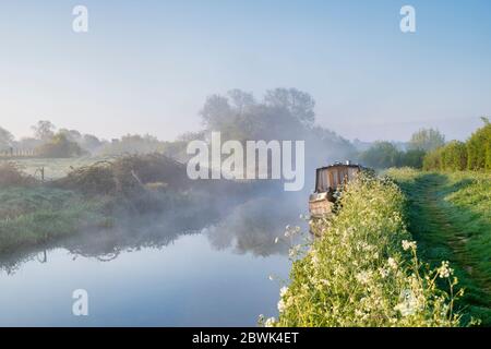 Narrowboat in the mist on the Oxford canal on a spring morning just after sunrise. Upper Heyford, Oxfordshire, England Stock Photo