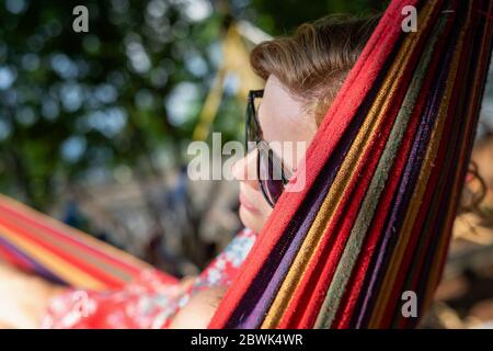 Outdoor portrait of young beautiful blonde cheerful girl enjoy in hammock outdoor. Relaxing in the hammock in the summer garden Stock Photo