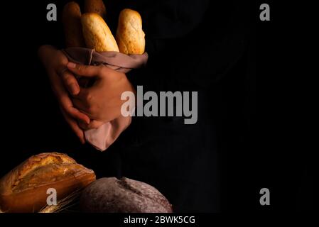 Woman holding tasty fresh breads on a dark. Baking and cooking concept background. Hands of baker carefully hold loaf on wooden table, sprinkled with Stock Photo