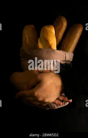 Woman holding tasty fresh breads on a dark. Baking and cooking concept background. Hands of baker carefully hold loaf on wooden table, sprinkled with Stock Photo