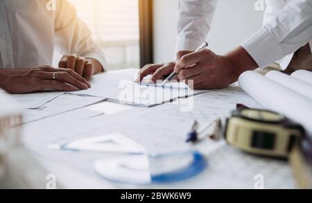 Architects engineer working with blueprints on table and discussing project together at the meeting in the office. Stock Photo