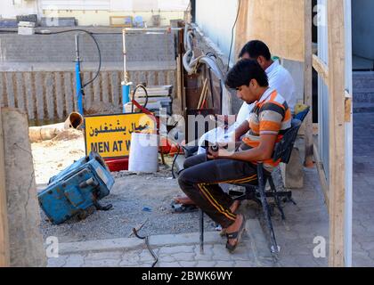 Two men sitting at construction site using mobile phone, Muscat, Oman Stock Photo