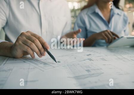 Architects engineer working with blueprints on table and discussing project together at the meeting in the office. Stock Photo