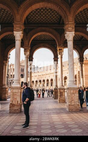 Seville, Spain - January 17, 2020: People walking amongst arches on Plaza de España, a plaza in the Parque de María Luisa, in Seville, Spain, built in Stock Photo