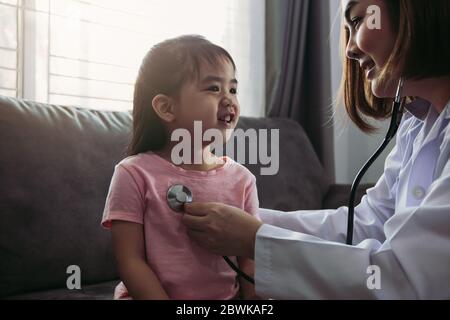 Confident asian woman healthcare professional visit her patient using a stethoscope during a young female patient well check at home.