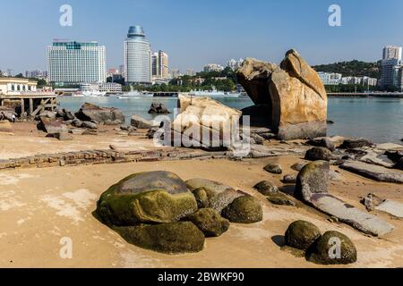 Big rocks on the sandy shore of Gulangyu Island. In the background anchoring ships and a view on the Xiamen skyline. Stock Photo