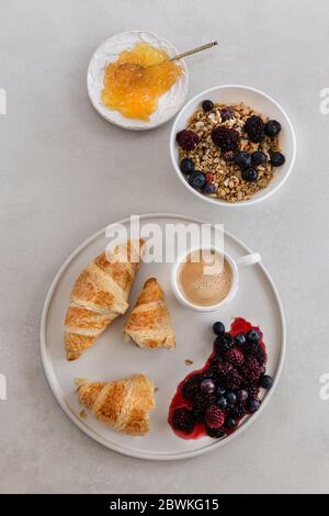 Topview image of healthy breakfast with coffee, granola, orange marmelade and berries in a minimalistic white flatware over light gray background. Stock Photo
